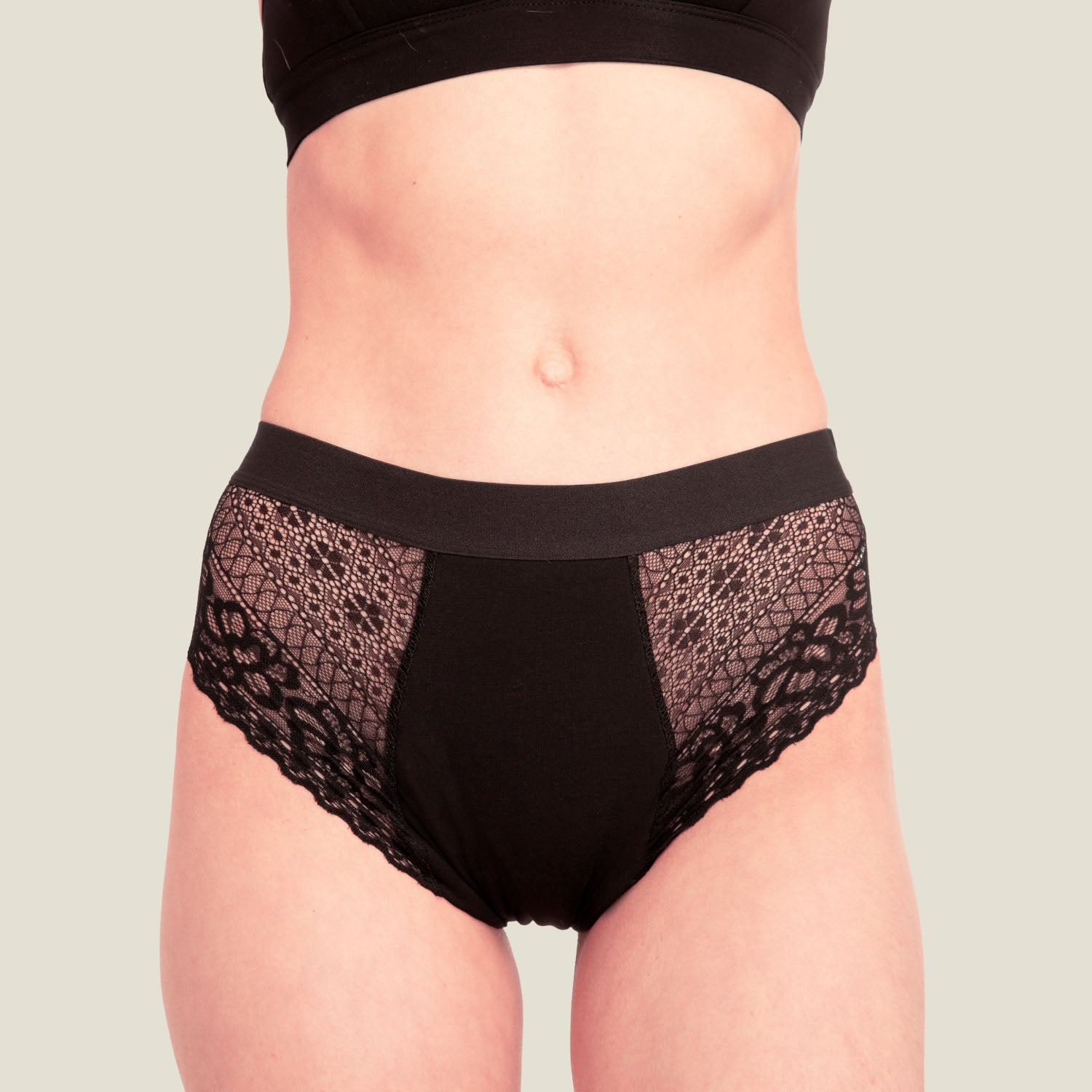 Model wearing WUKA Ultimate™ Lace Hipster Brief in black for medium flow, shown full-length with matching black bra, highlighting breathable period underwear with lace side panels and mid-rise fit.