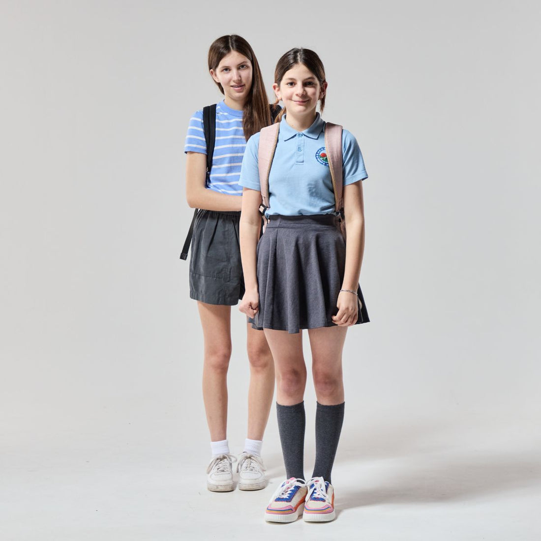 two girls in school uniform stand smiling at the camera 
