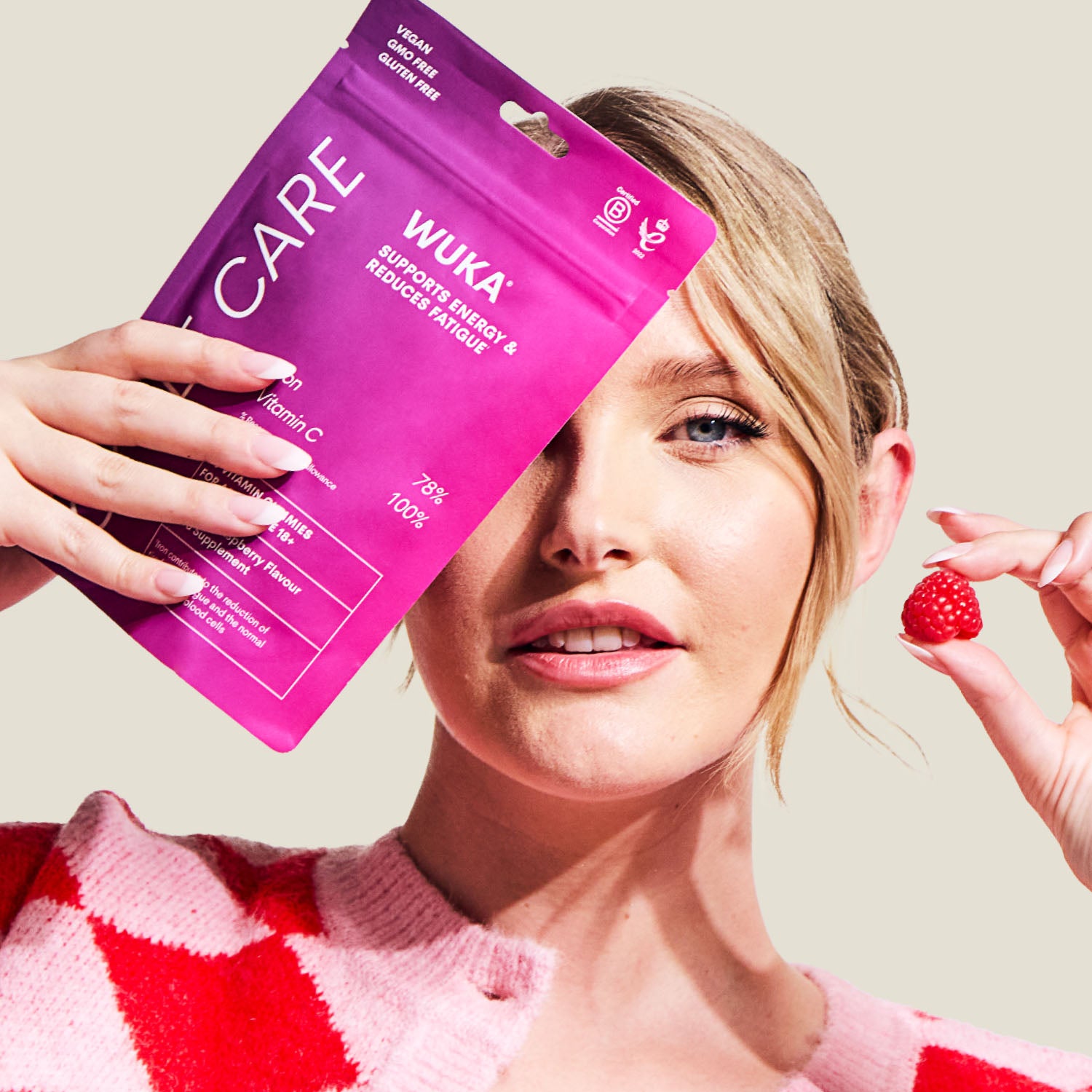 WUKA adult iron support gummies held by woman smiling with raspberry gummy in hand – energy and fatigue support supplement.